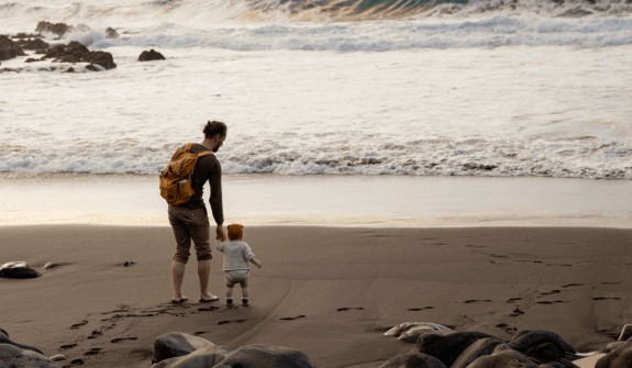 Dad with toddler on beach walking towards surf