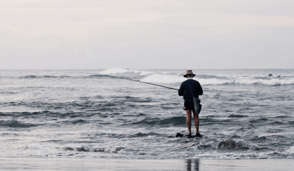 Man fishing in shallows at surf beach